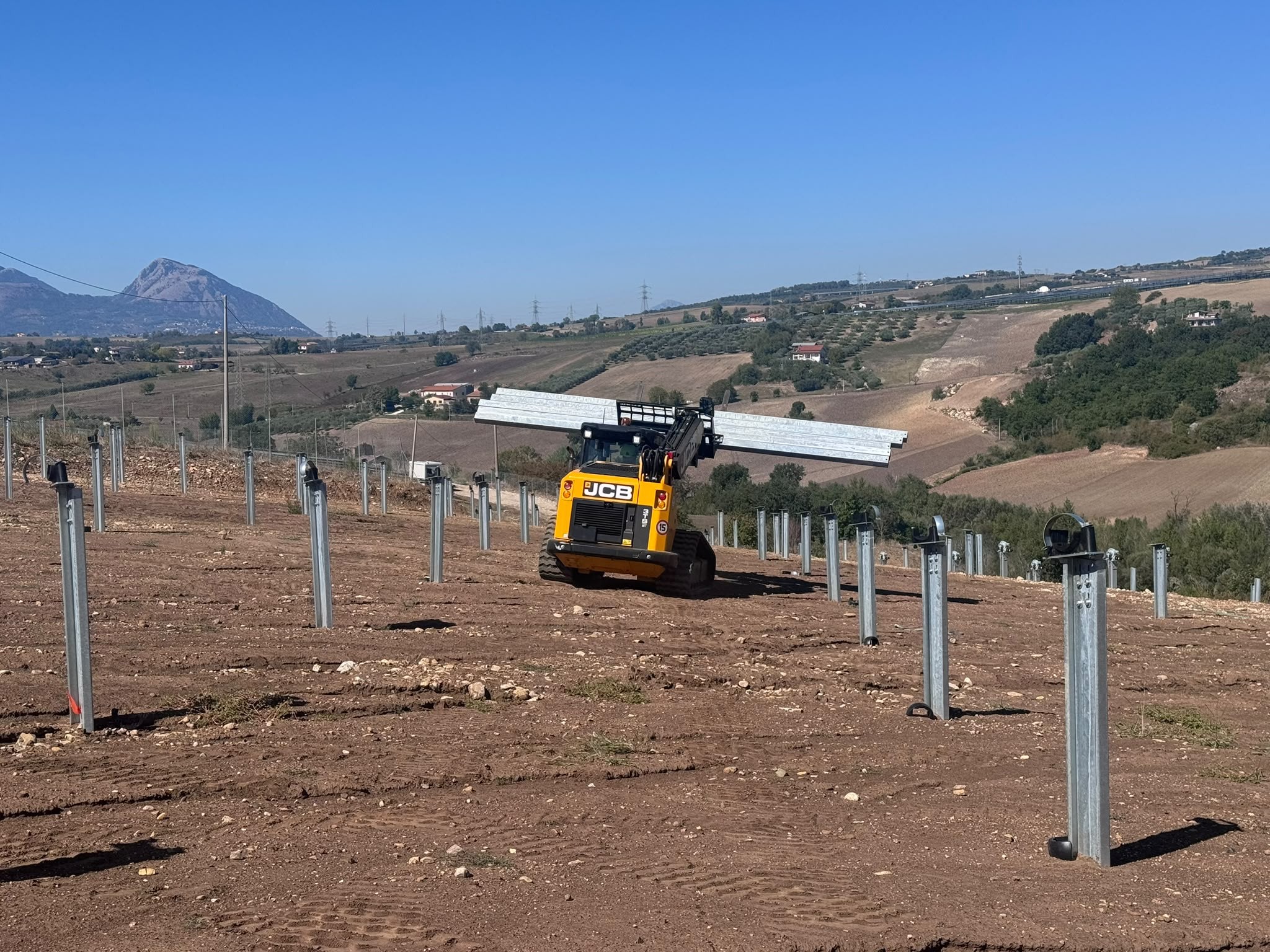 Cantiere di un impianto a terra con pali infissi e sollevatore telescopico