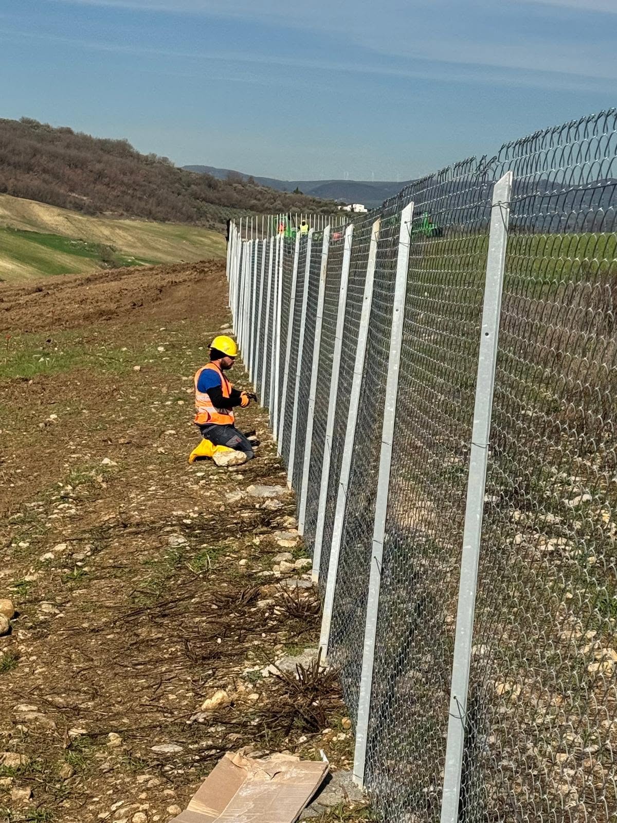 Tecnico con DPI durante la posa di una recinzione in un impianto a terra